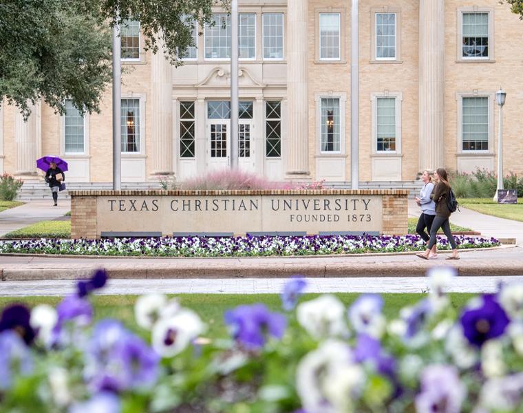 View of Texas Christian University sign and Sadler Hall from flower beds across University Drive