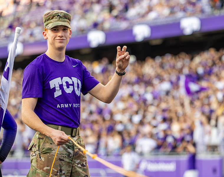 TCU ROTC student at a football game throwing up the go frogs hand sign 