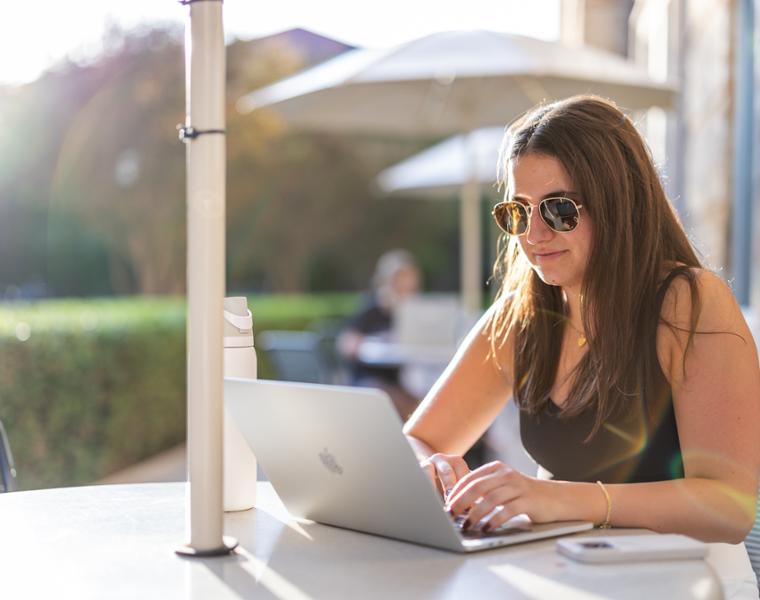 Female student on computer outside on campus.