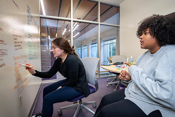 Two students notetaking on a whiteboard