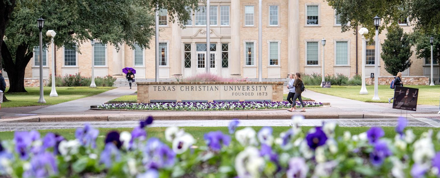View of Texas Christian University sign and Sadler Hall from flower beds across University Drive