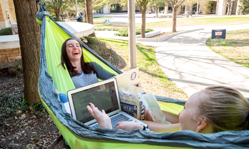 Girls laughing in a hammock while looking at a laptop screen 